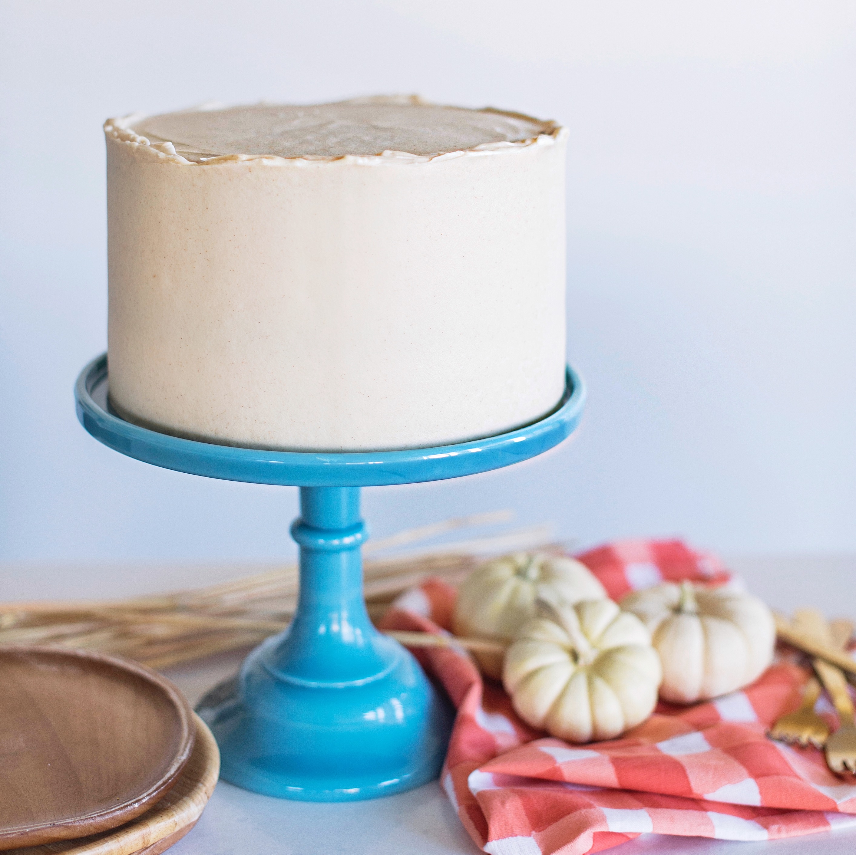 Cake on a cake stand with pumpkins on the table. 