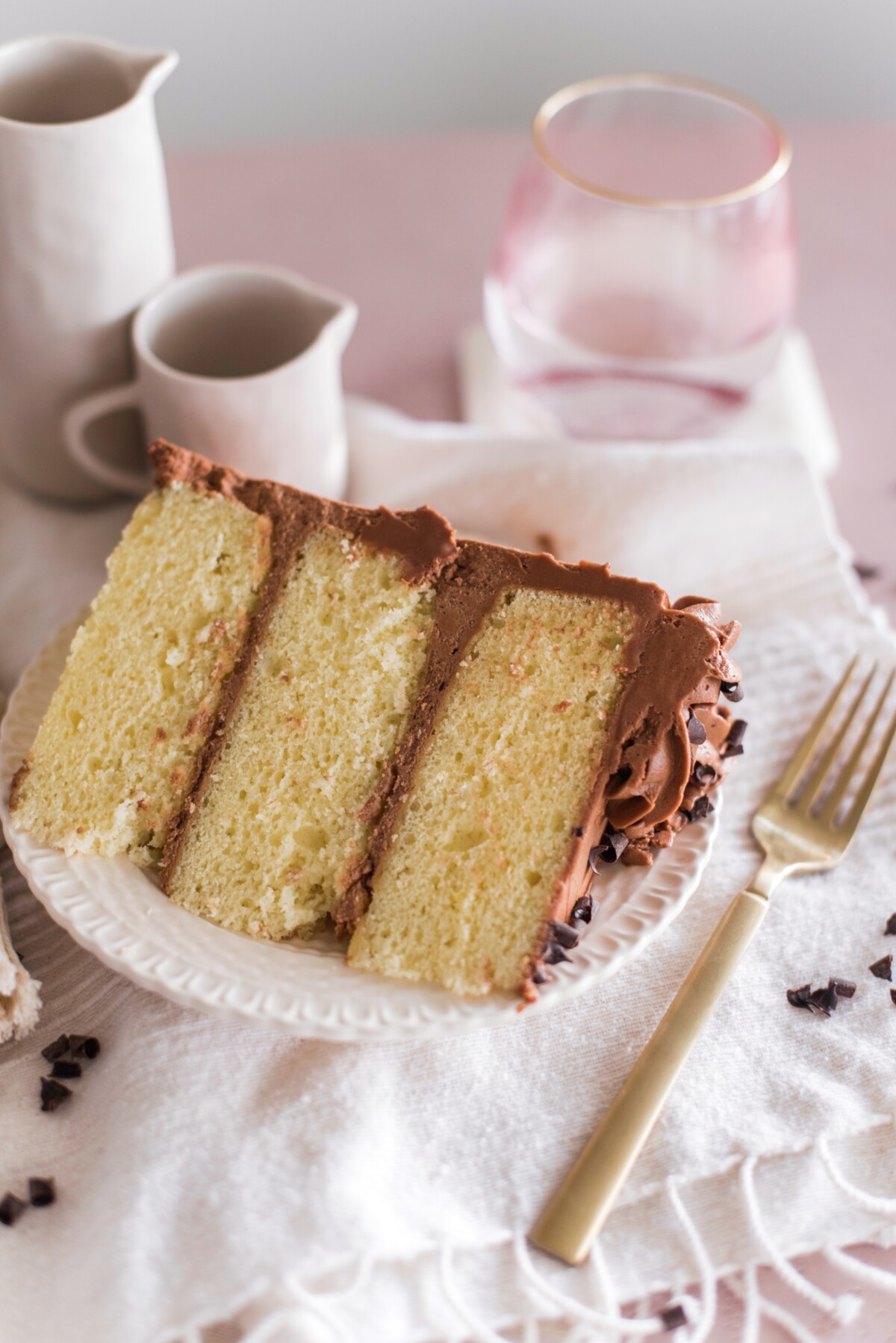 A slice of yellow cake with chocolate buttercream with a pink table and accessories.