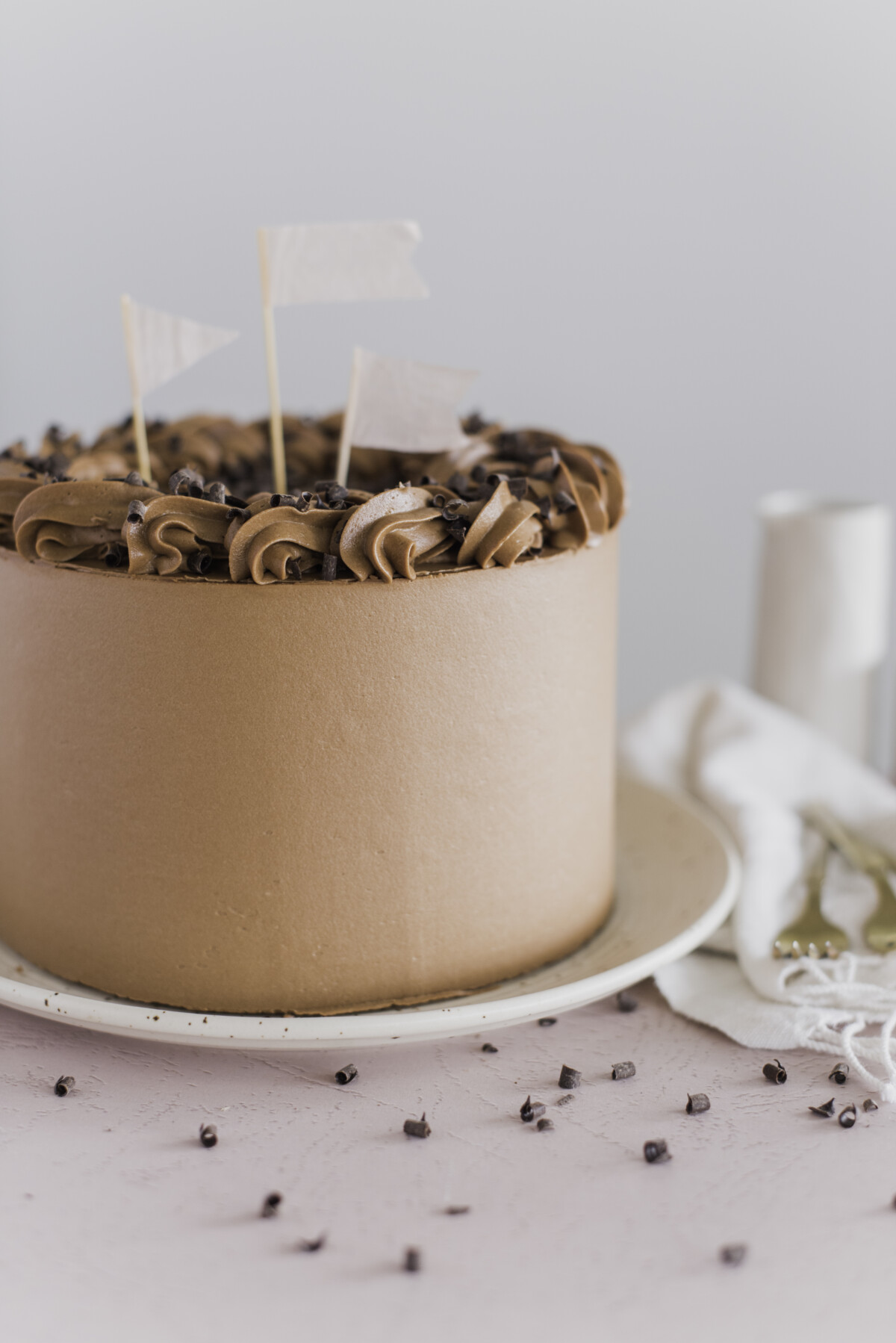 A yellow layered cake with chocolate buttercream on a plate, with decorations on it.