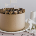 A yellow layered cake with chocolate buttercream on a plate, with decorations on it.