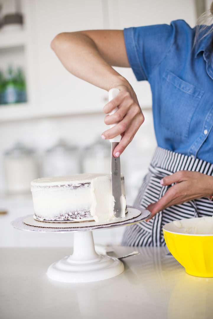 Woman adding buttercream to a cake with an icing spatula.