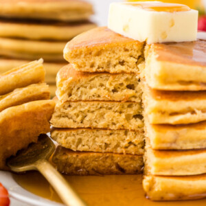 A stack of light and fluffy pancakes with a bite taken out and fork on the plate.