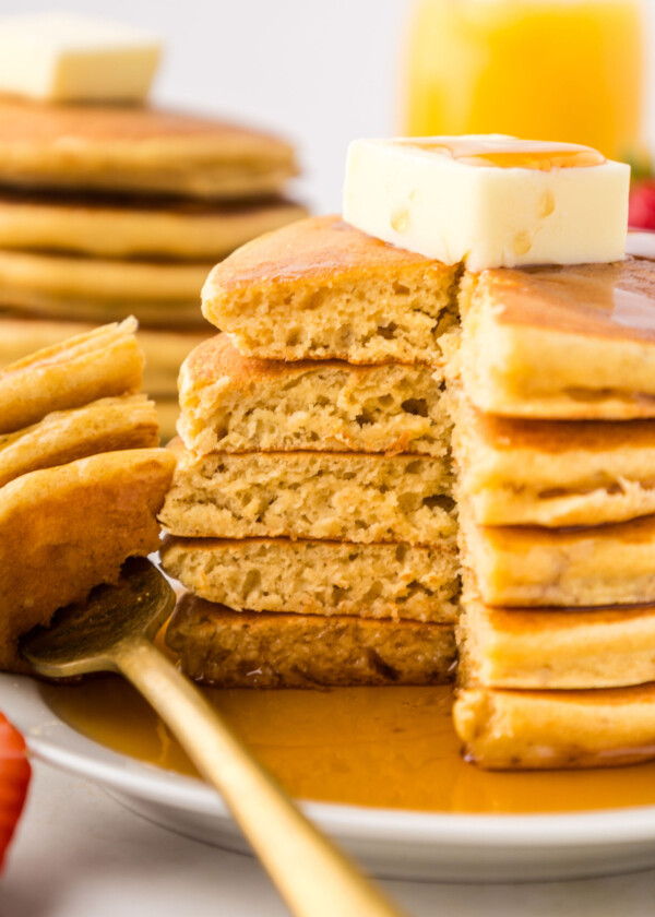 A stack of light and fluffy pancakes with a bite taken out and fork on the plate.