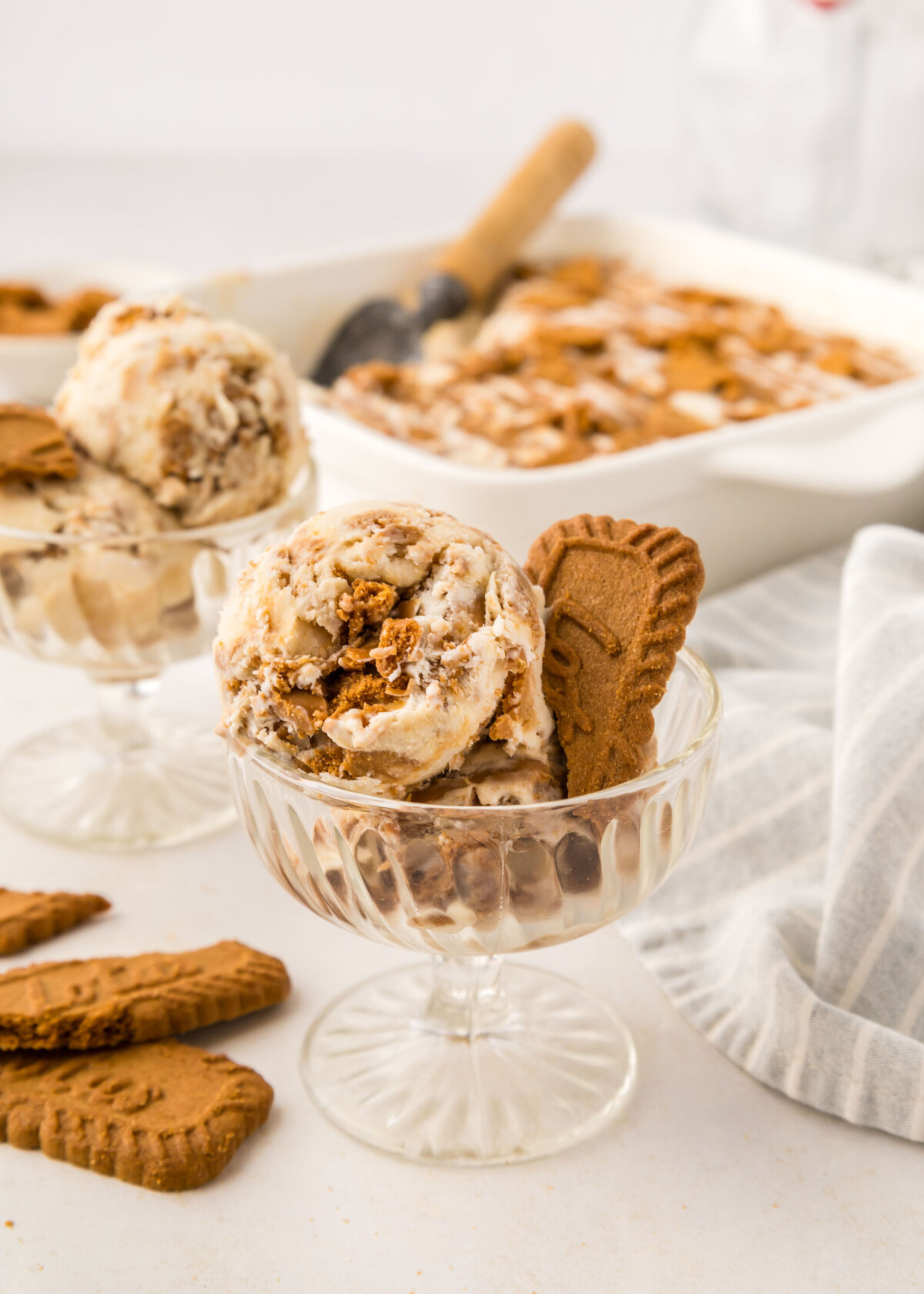 Homemade Biscoff ice cream in a cup with ice cream behind it and cookies on the table.