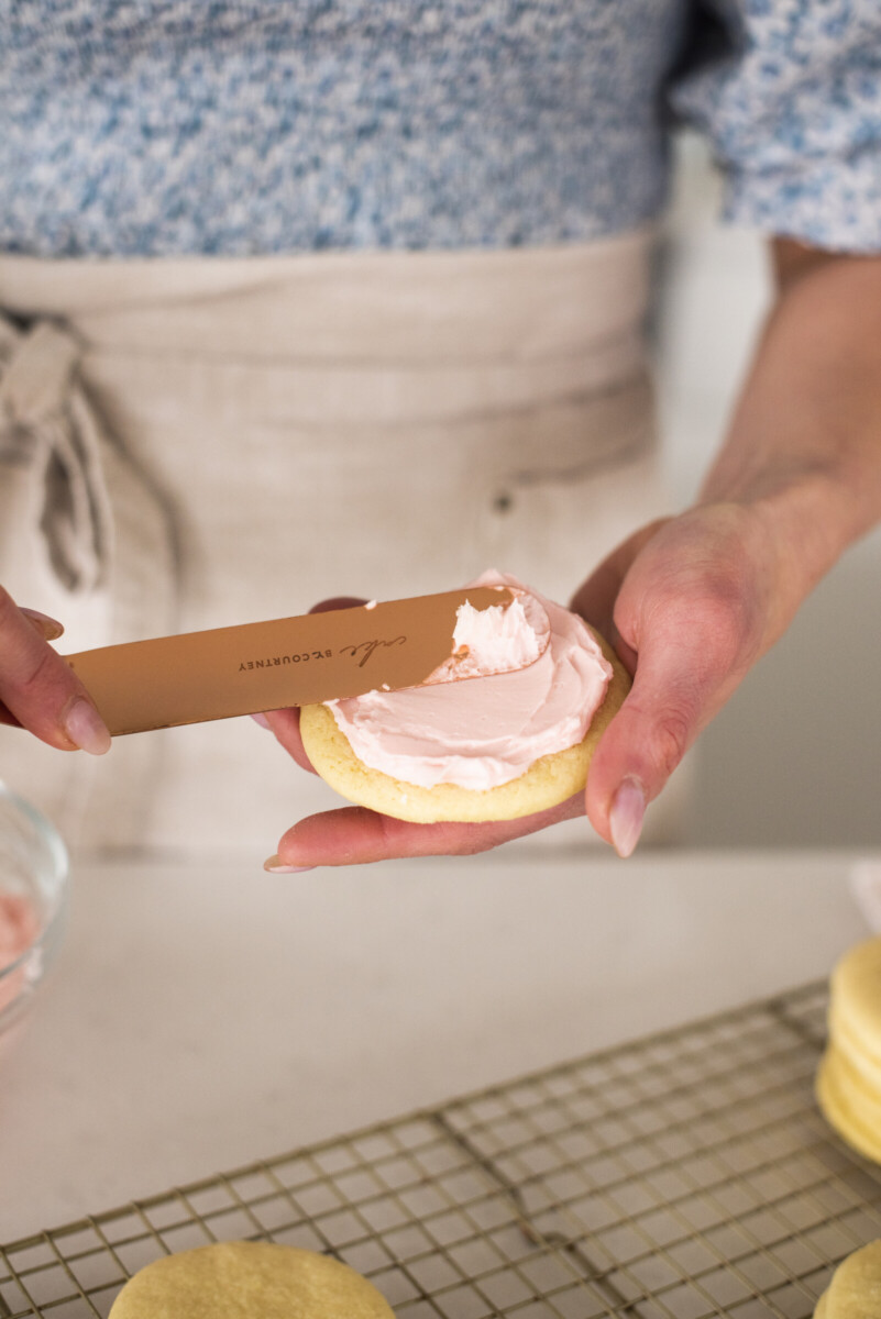 A woman frosting a sugar cookie with pink buttercream.