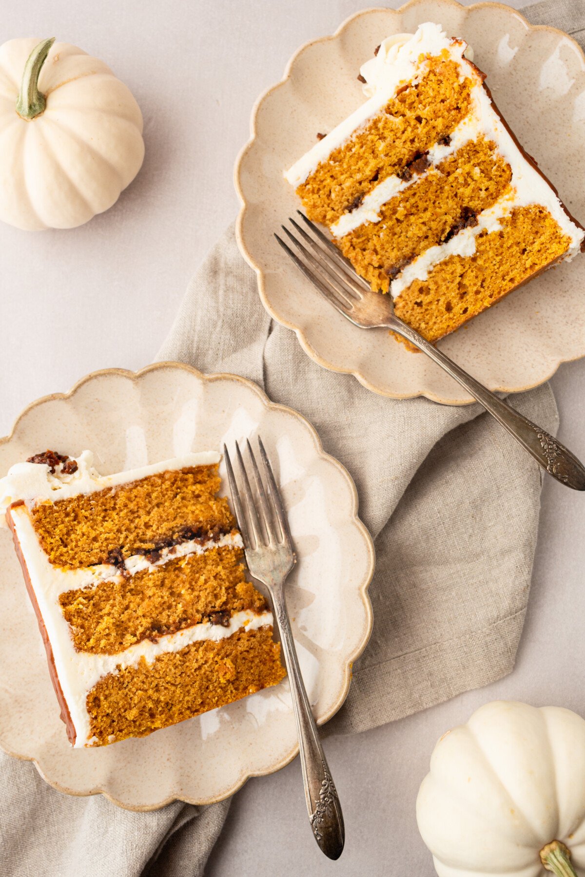 Two slices of cake on plates with white pumpkins next to them.