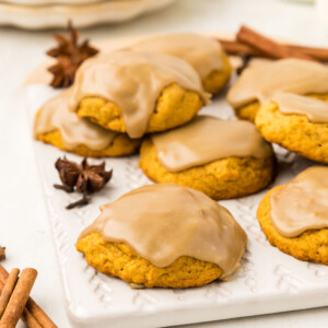 Pumpkin cookies on a cutting board with cinnamon sticks.