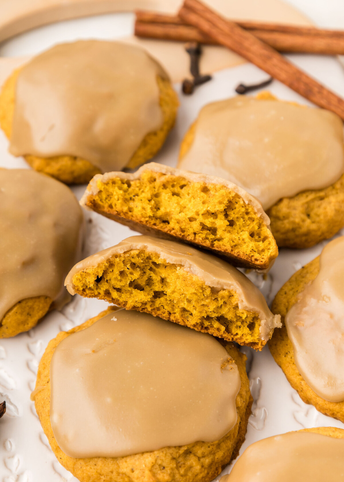 Pumpkin cookies with a maple glaze cut in half with cinnamon sticks.