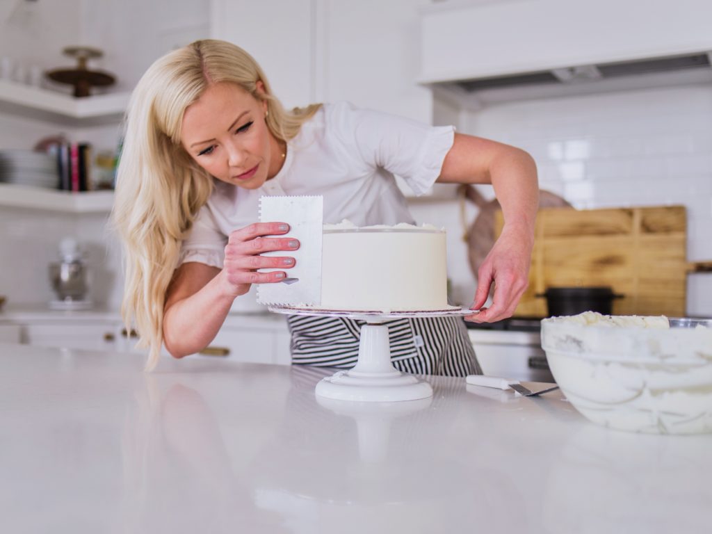 Female baker spreading icing on a layered cake