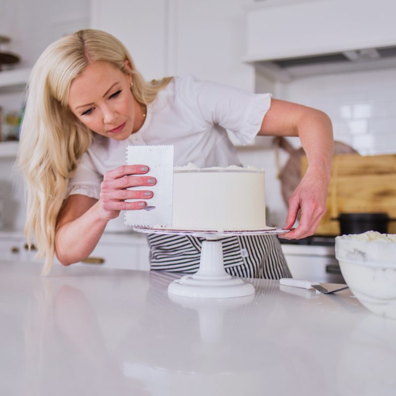 Female baker carefully spreading buttercream icing on a layered cake