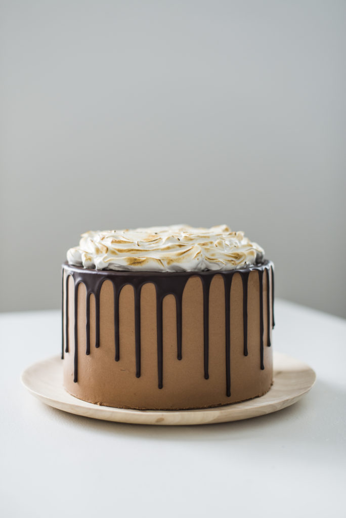 Chocolate s’mores cake with toasted marshmallow on top and a chocolate ganache dripping down the sides