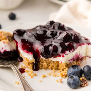 Blueberry delight bar on a plate with a bite taken out of it on a fork.