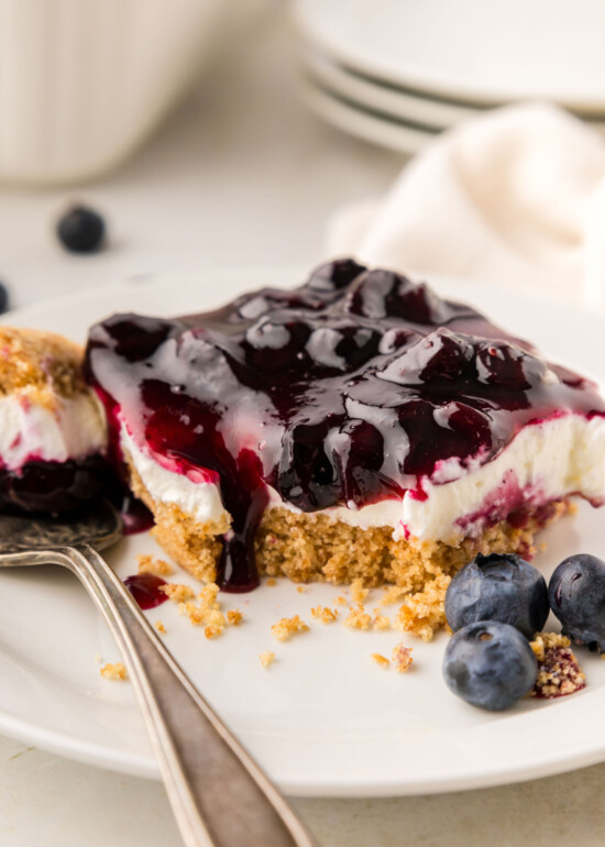 Blueberry delight bar on a plate with a bite taken out of it on a fork.