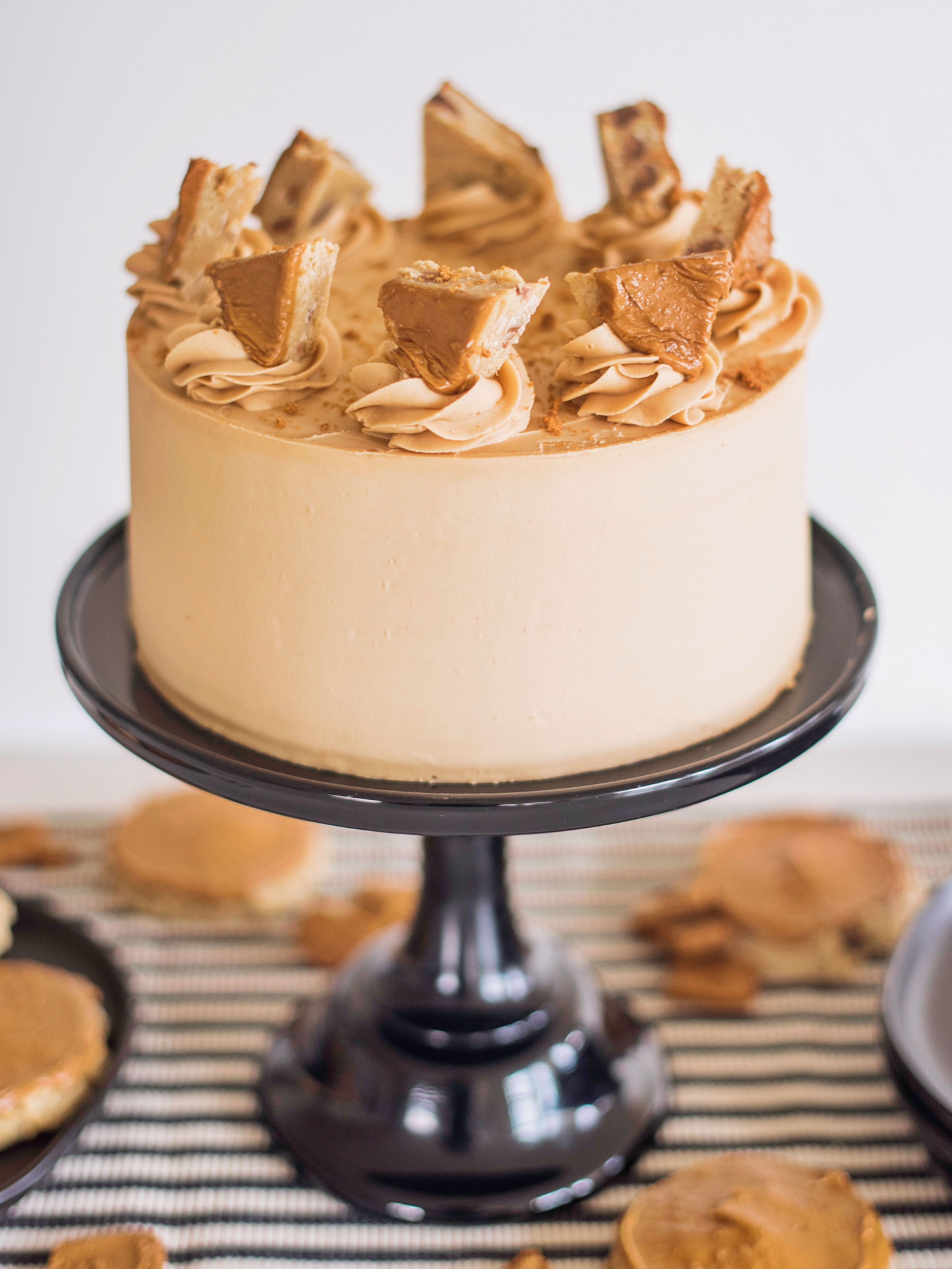 Biscoff cake on a black cake stand with cookies.
