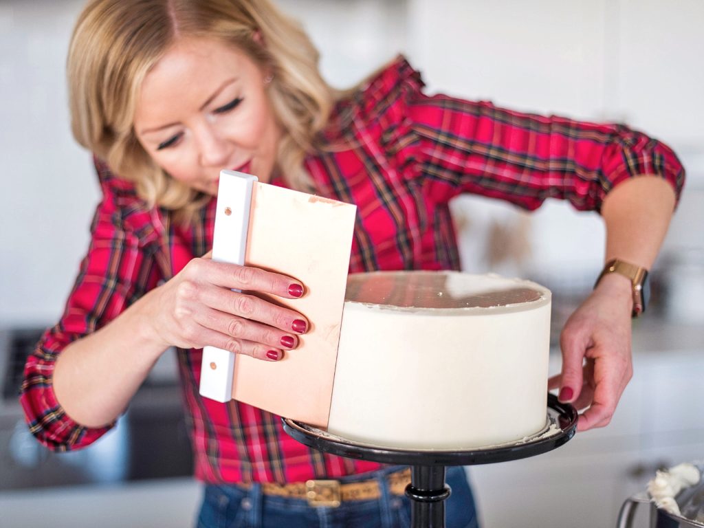 Woman using a cake scraper to smooth the sides of a cake.