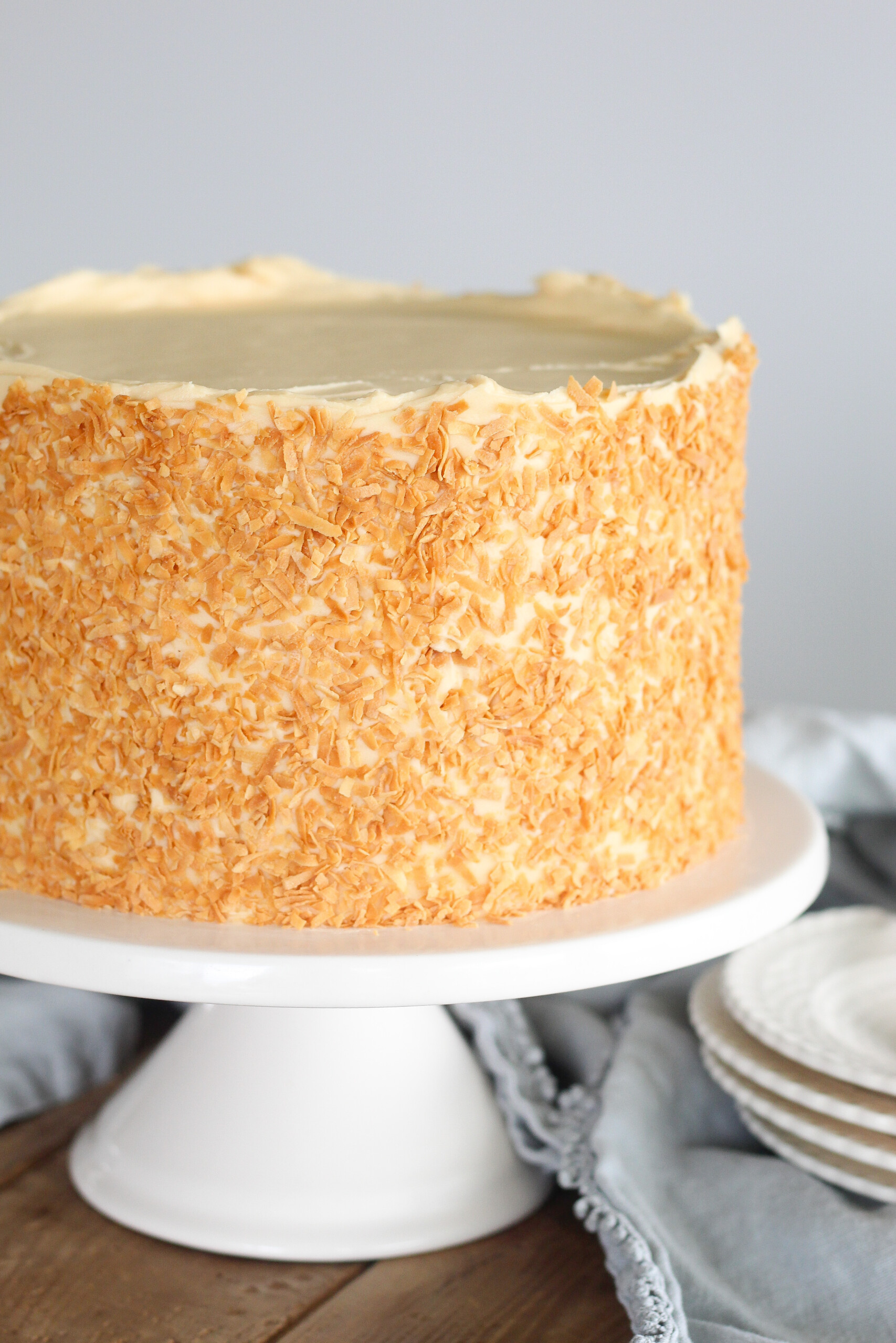 Coconut Caramel Cake covered in toasted coconut on a white cake stand.