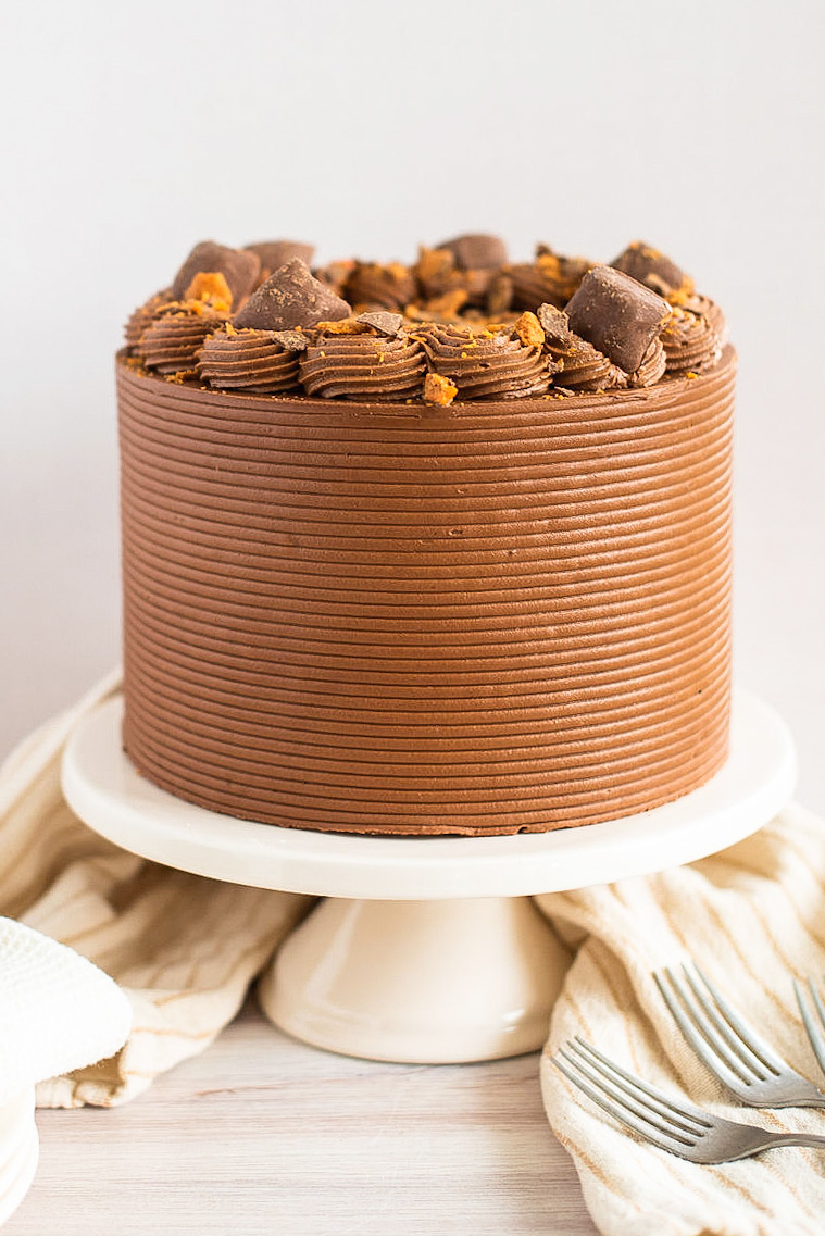 A chocolate peanut butter Butterfinger Cake on a cake stand.