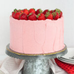A pink strawberry cheesecake cake on a metal cake stand with plates.