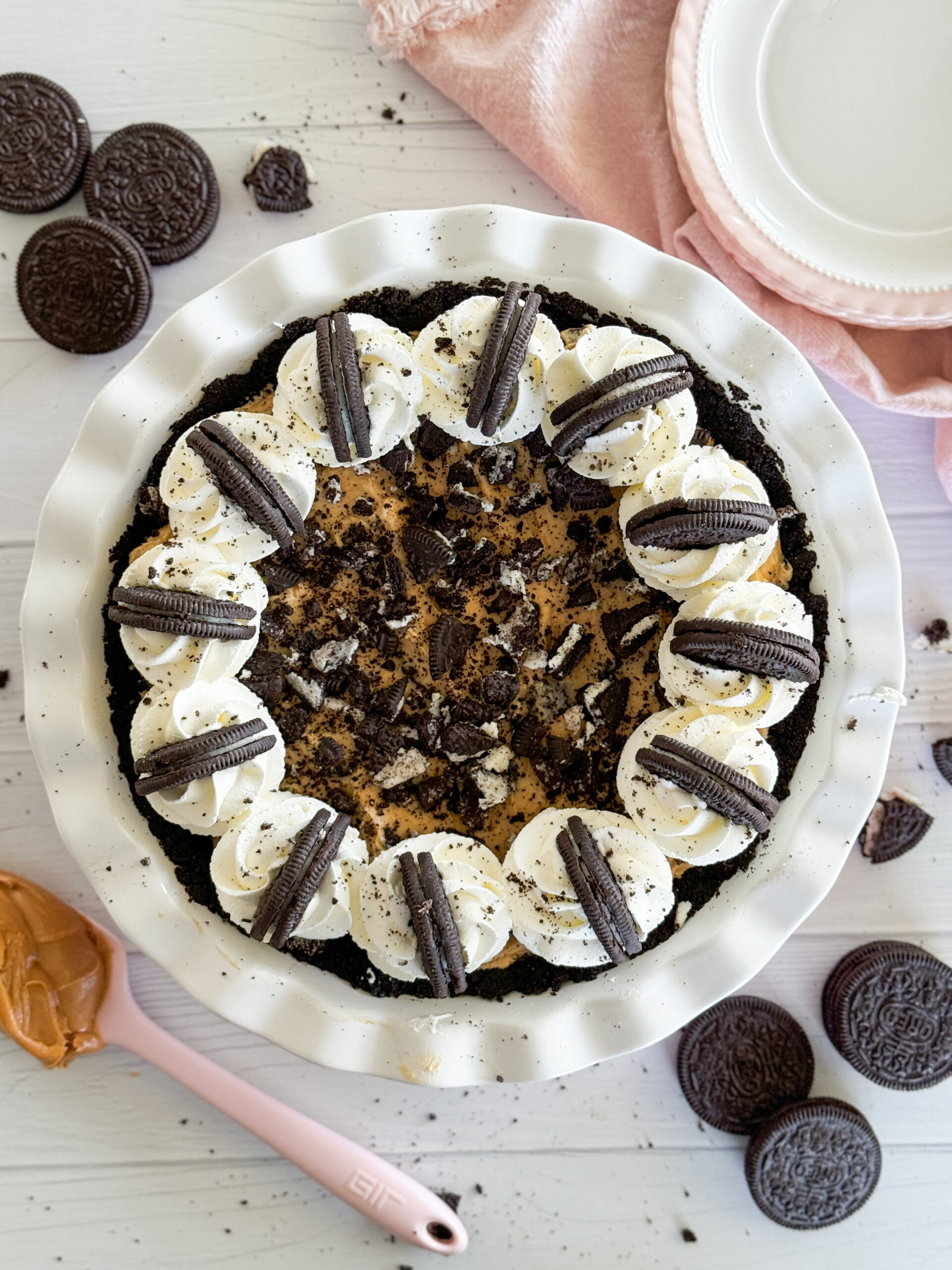 A peanut butter Oreo pie in a pie dish with plates and Oreos on the table.