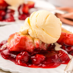 Scoop of cherry cobbler on a plate with ice cream.