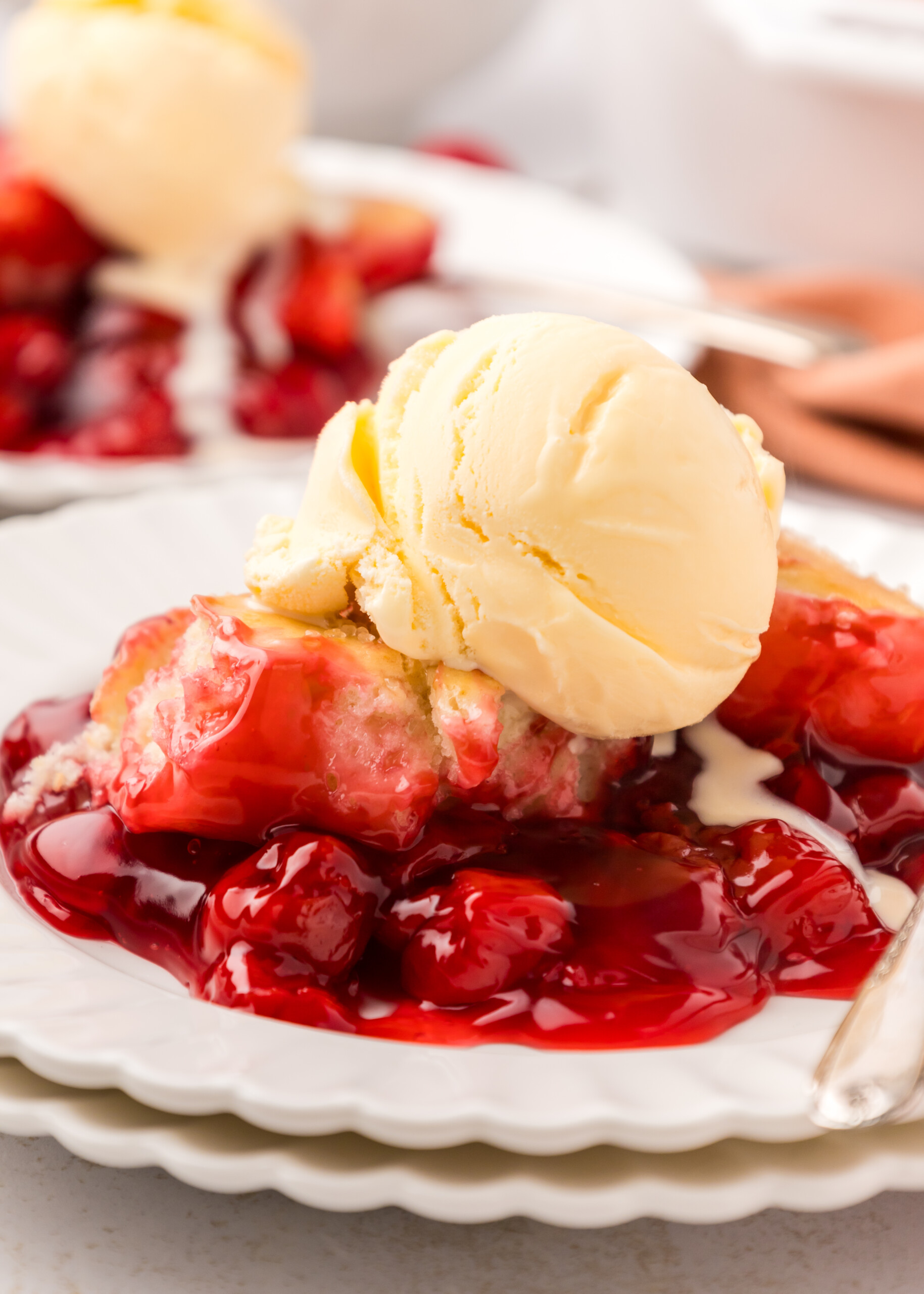 Scoop of cherry cobbler on a plate with ice cream.