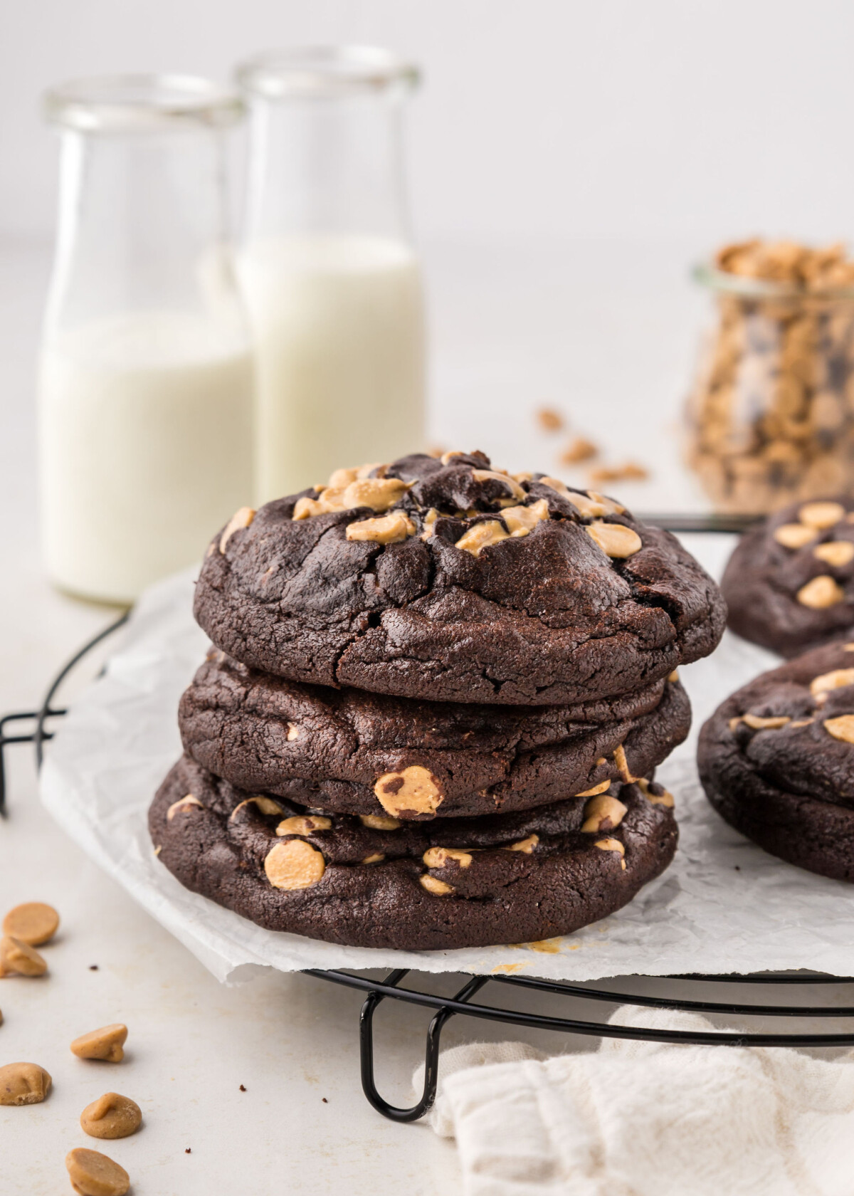 Stack of three cookies on a cooling rack with glasses of milk.