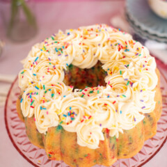 A confetti bundt cake with vanilla buttercream on a pink cake stand.