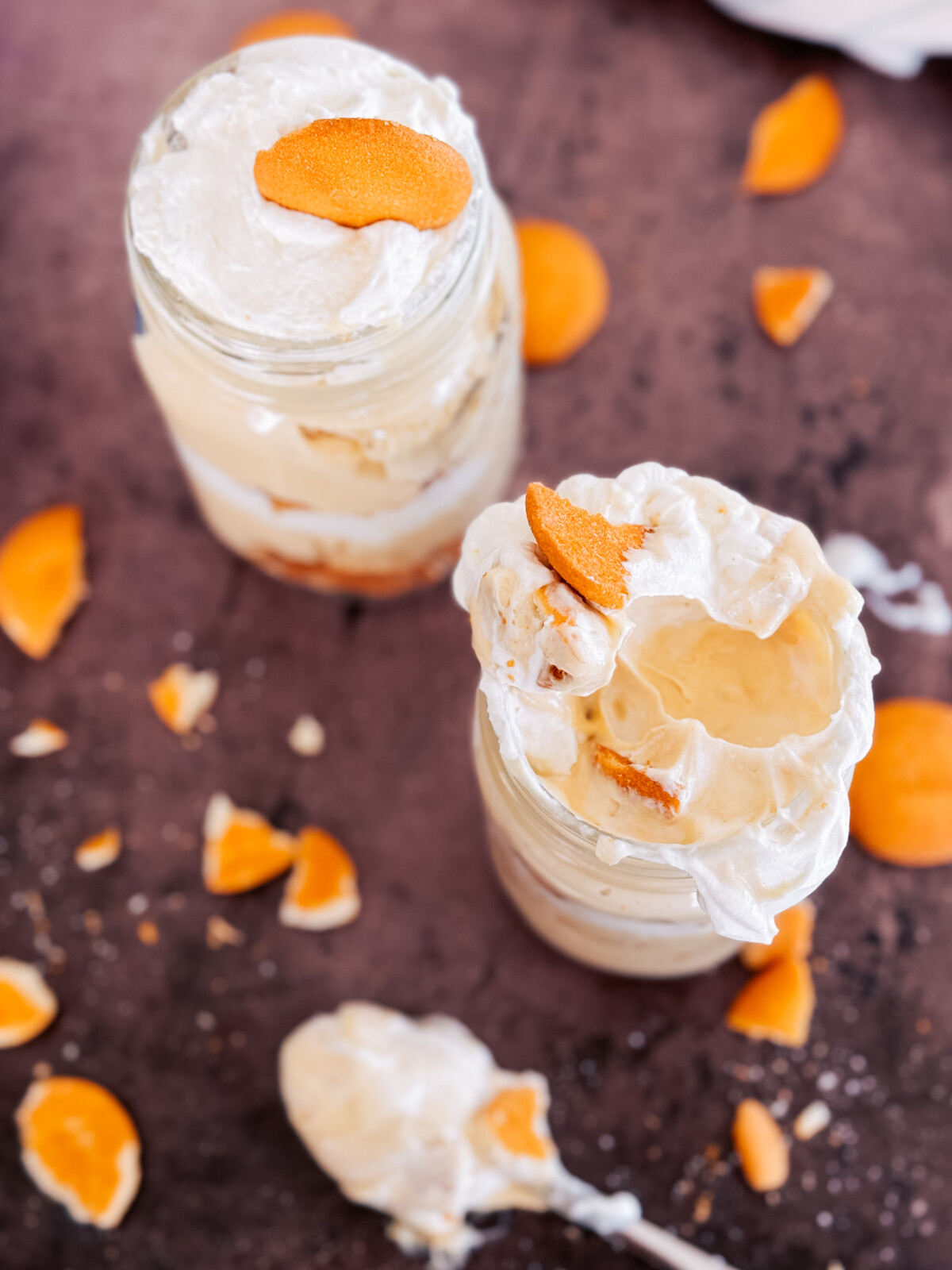 Two jars of peanut butter banana pudding on a table with cookies and a spoon.