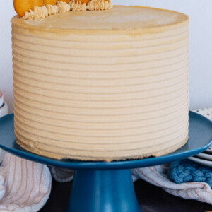 A tall layered cake on a blue cake stand with Nilla Wafer cookies and plates next to it.