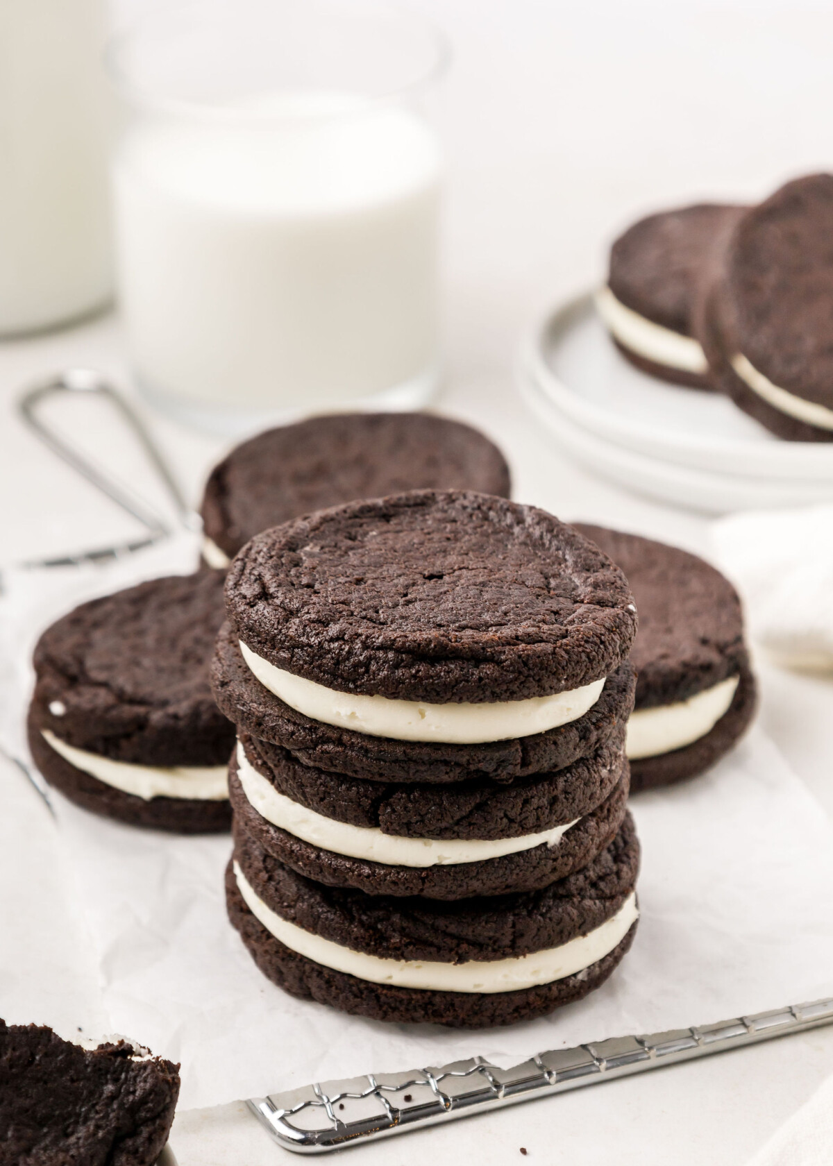 A stack of homemade Oreo cookies with cookies and milk nearby.