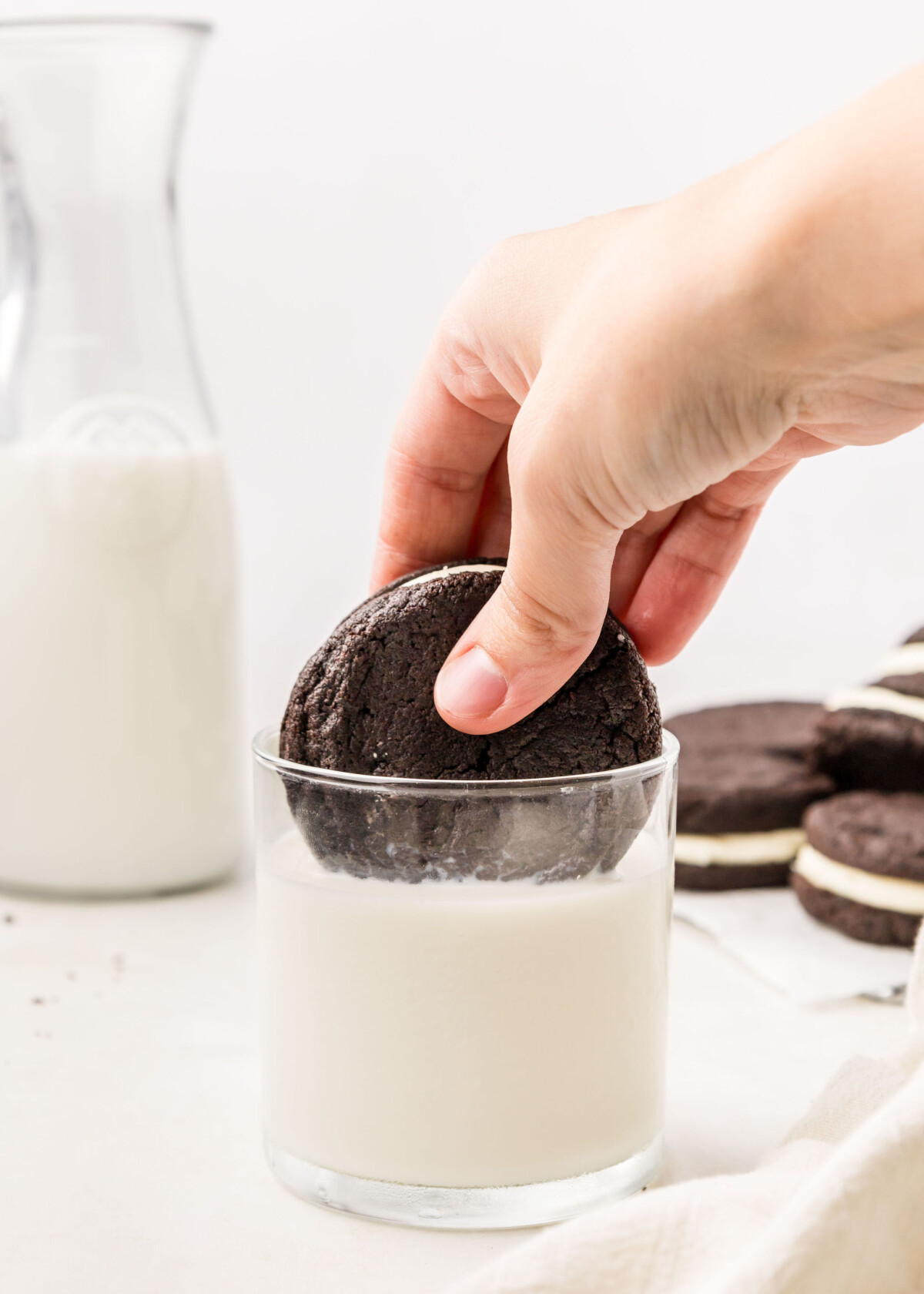 A person dipping an homemade Oreo cookie into a class of milk.