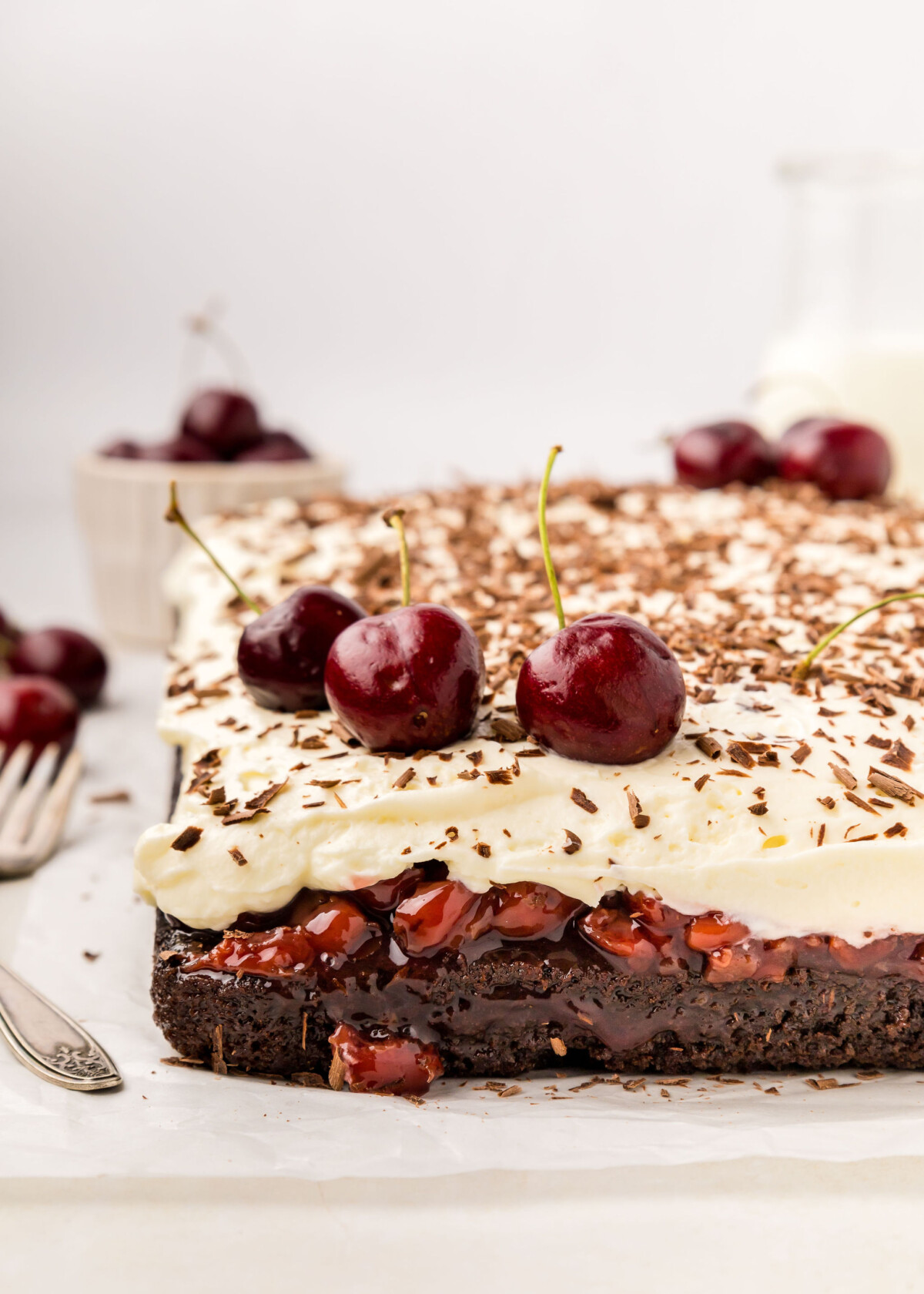 A sheet cake with whipped cream, cherries and chocolate shavings on it.