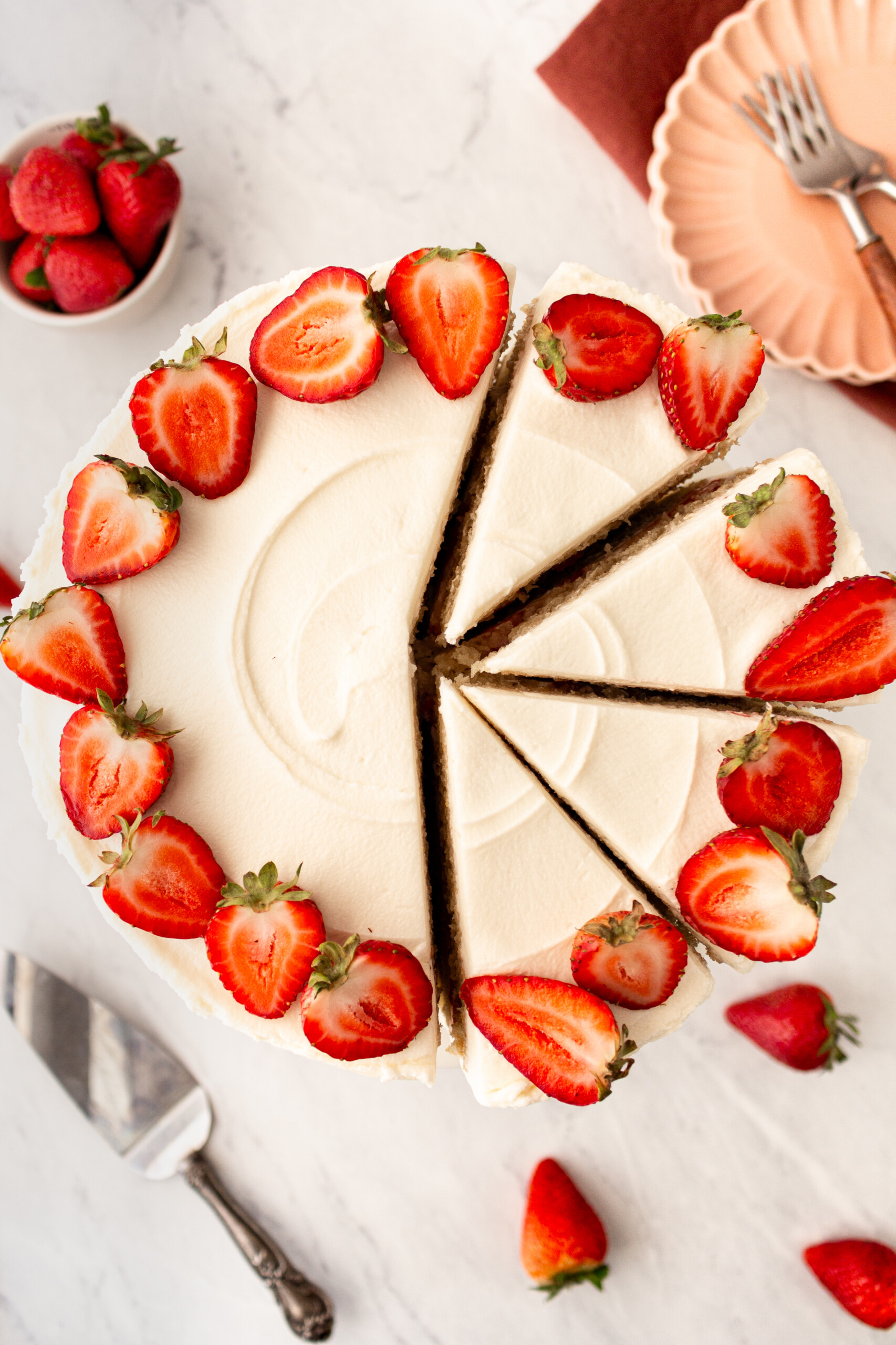 A vanilla cake with vanilla frosting cut into four slices with strawberries on it.