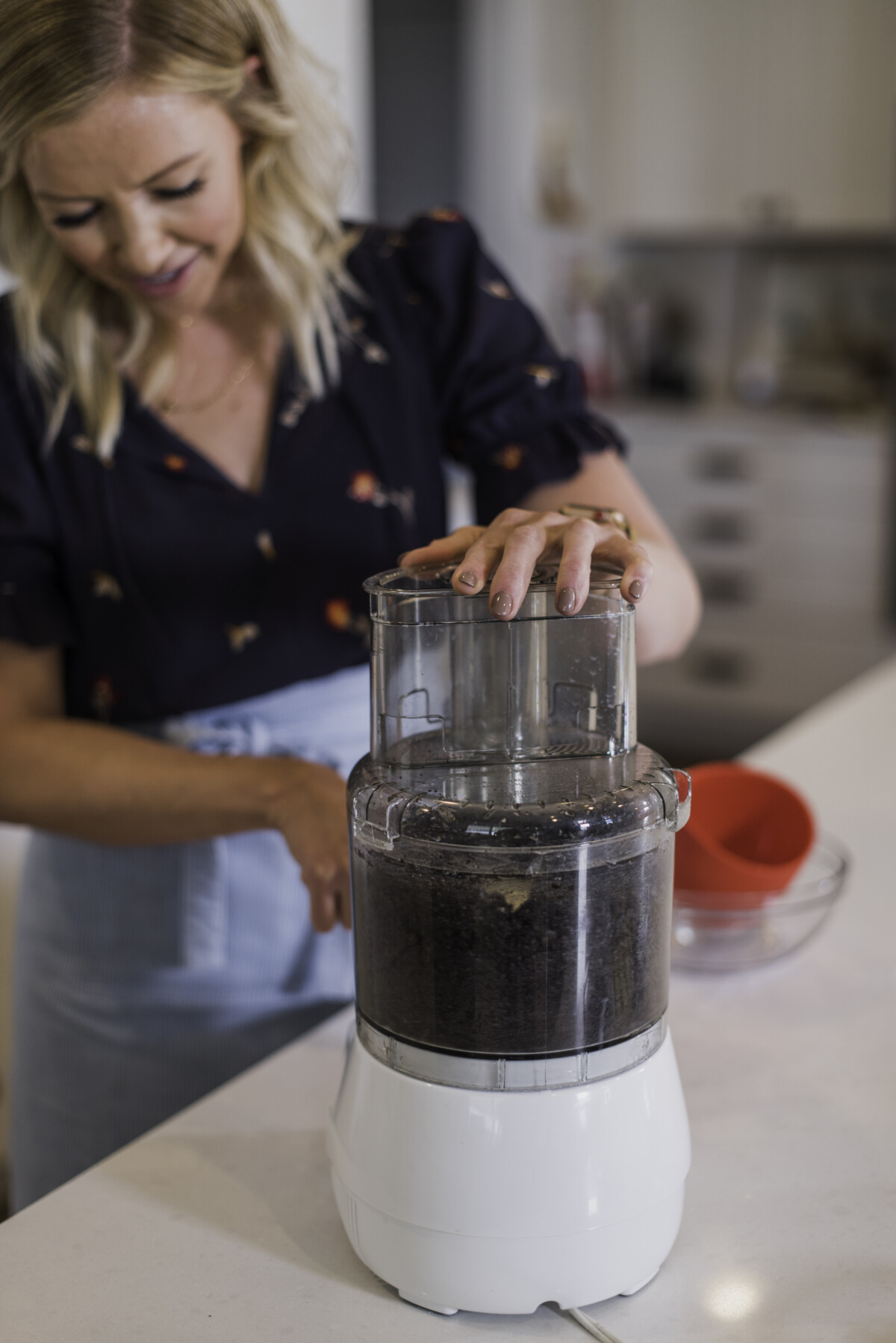 A woman using a food processor to make an Oreo cookie crust.