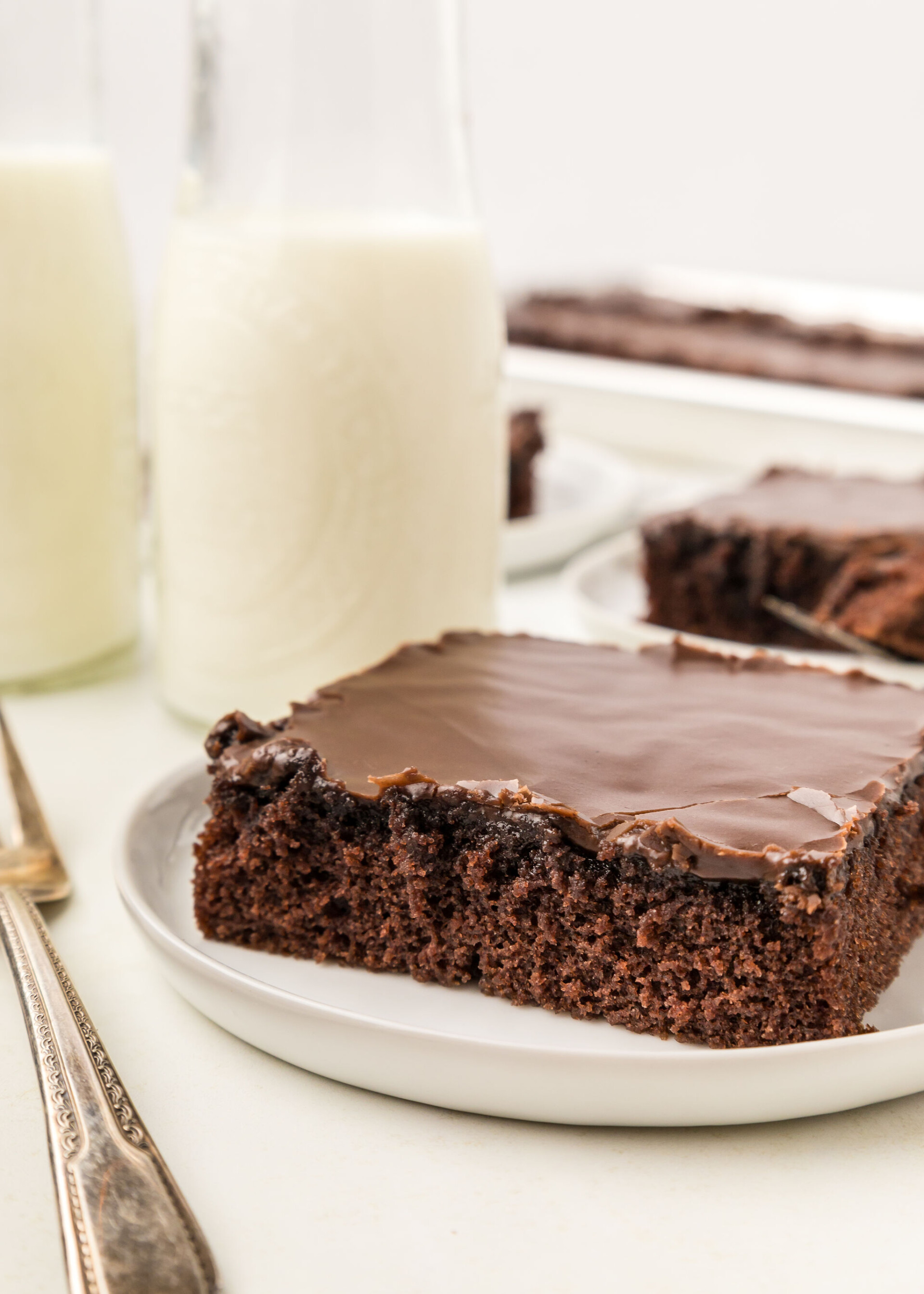 A slice of Texas Sheet Cake on a plate with a glass of milk.