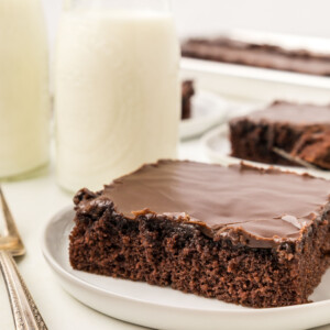 A slice of Texas Sheet Cake on a plate with a glass of milk.