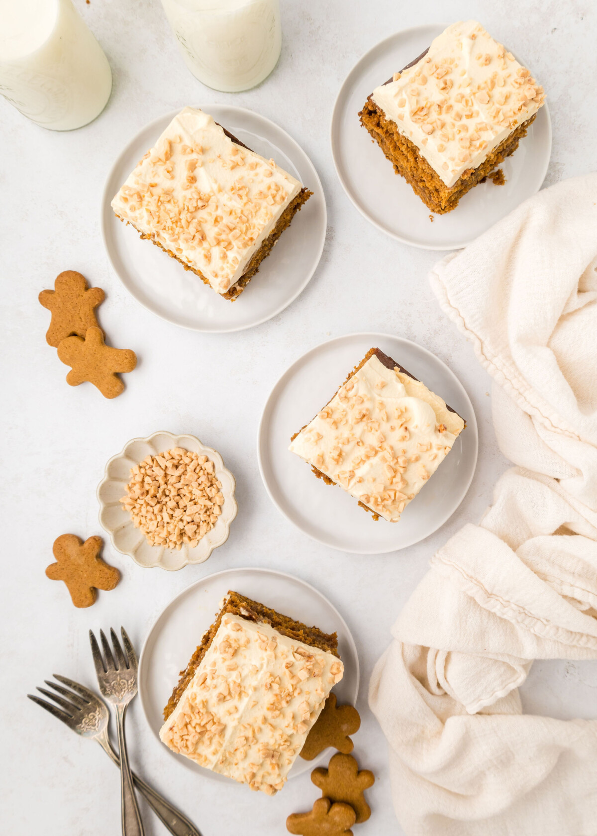 Four slices of cake on plates with gingerbread cookies, forks and napkins on the table.