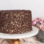 A chocolate cake with brown sugar buttercream on a cake stand.