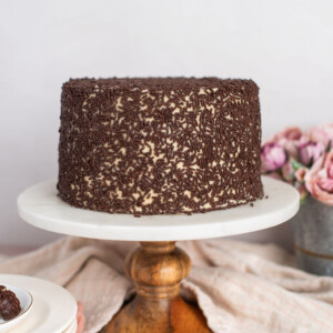 A chocolate cake on a cake stand with chocolate sprinkles.