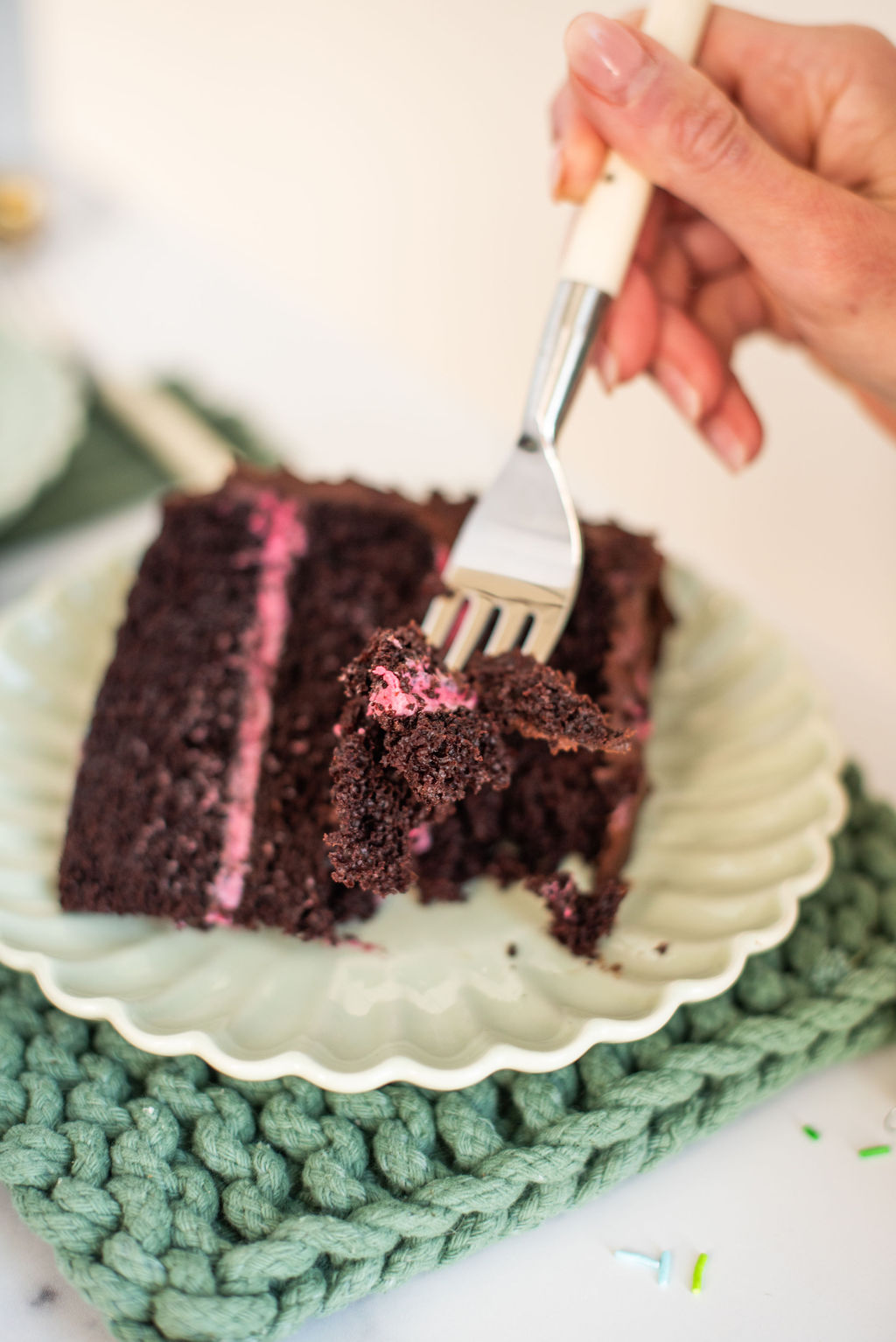 A woman holding a fork that has a bite of chocolate cake on it.