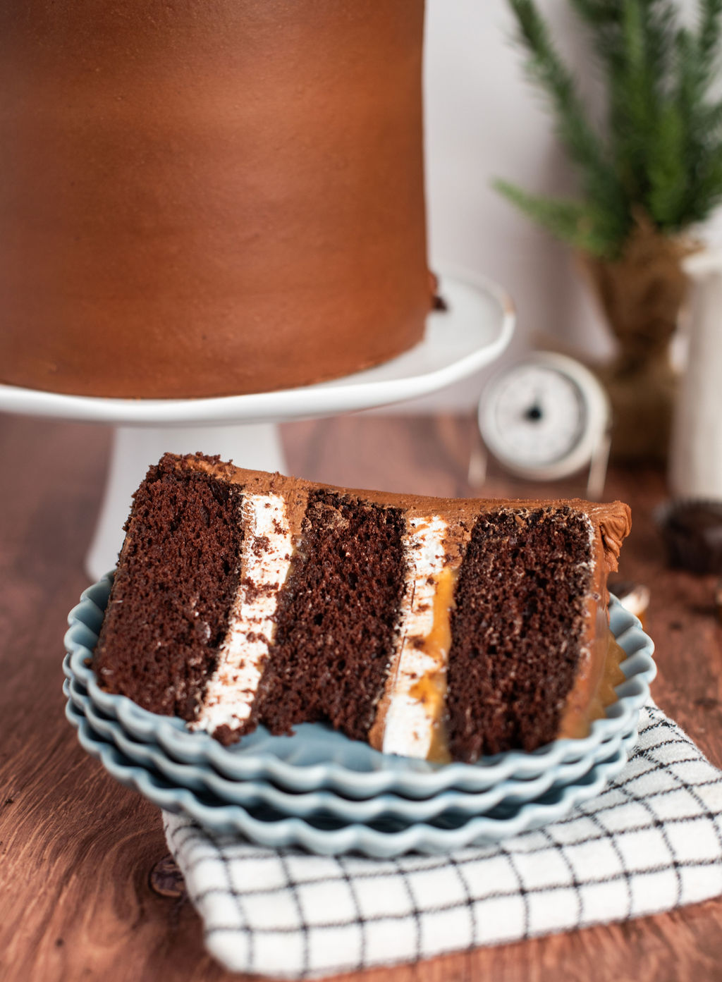 A slice of chocolate cake with marshmallow, caramel and chocolate buttercream on a stack of plates.