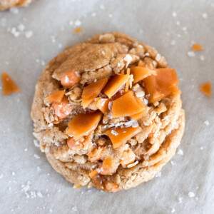 A single oatmeal butterscotch salted caramel cookie on a parchment sheet.