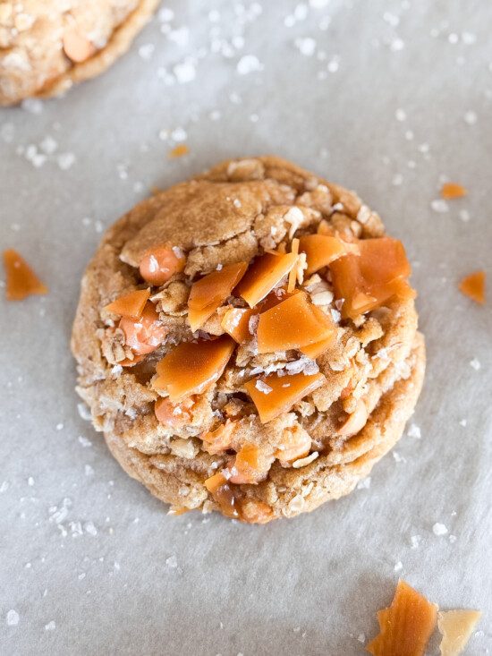 A single oatmeal butterscotch salted caramel cookie on a parchment sheet.