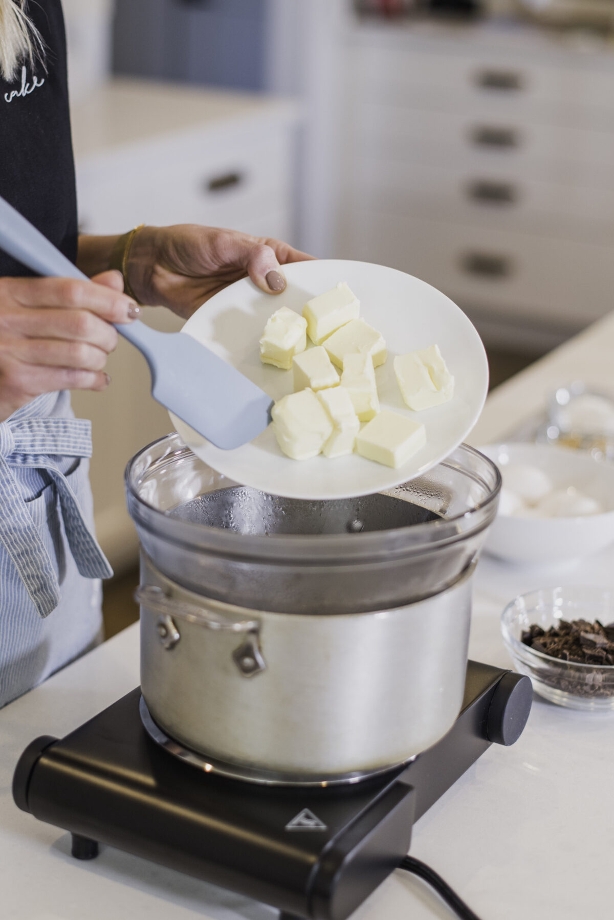 A woman melting butter in a double broiler.