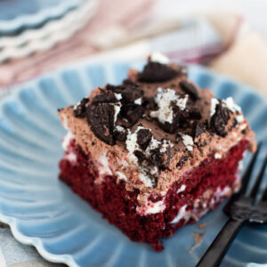 A slice of red velvet Oreo poke cake on a blue scalloped plate with a black fork.