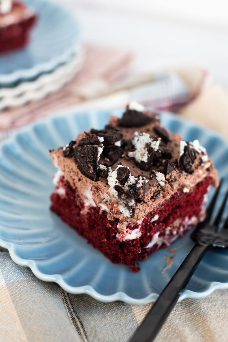 A slice of red velvet Oreo poke cake on a blue scalloped plate with a black fork.