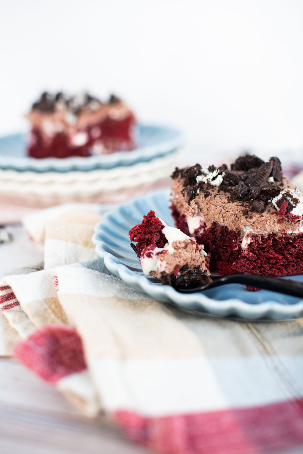 A slice of red velvet Oreo poke cake on a blue scalloped plate with a black fork.