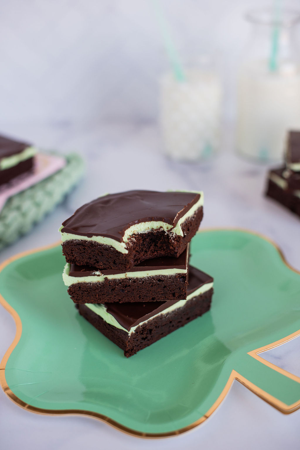 Three mint brownies in a stack on a green paper plate.