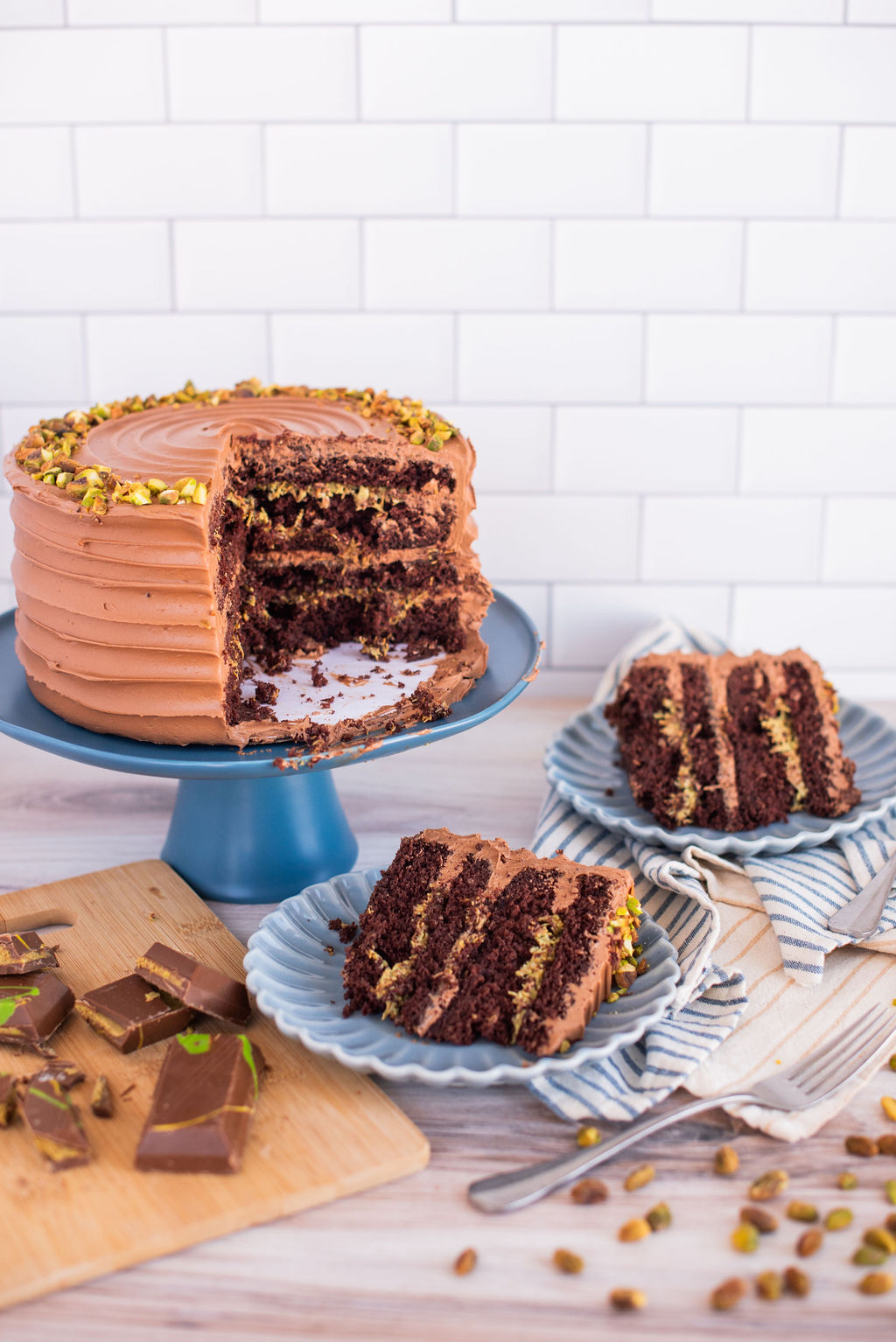 Two slices of cake on blue plates with a cake on a cake stand.