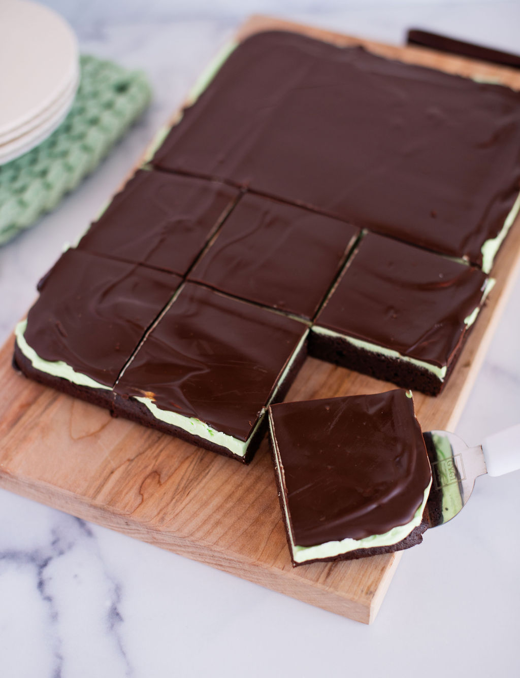 A batch of mint brownies on a cutting board with one slice removed to the side.